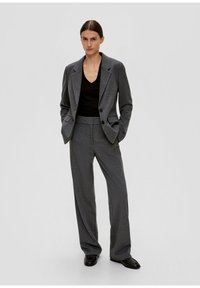 Blazer gris cintré avec des boutons sur le devant, associé à un haut noir ajusté et un pantalon large gris assorti, porté avec des chaussures noires.