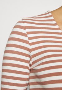 Gestreiftes Oberteil in einer Mischung aus Rost und Weiß, aus weichem Baumwollstoff, mit V-Ausschnitt und kurzen Ärmeln in enganliegender Silhouette.