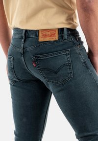 Jeans de mezclilla azul oscuro con un corte ajustado, que cuentan con bolsillos traseros, un diseño cosido y una etiqueta de cuero marrón en la pretina.