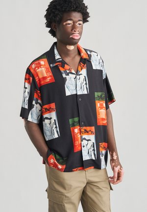 Camisa negra de manga corta con estampados llamativos y coloridos de vehículos y figuras, confeccionada con tela ligera y un ajuste relajado.