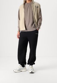 Fleecetröja, beige; grå sweatshirt; svarta mjukisbyxor; vita sneakers med ljusblå detaljer; avslappnad passform; minimal märkning på plaggen.