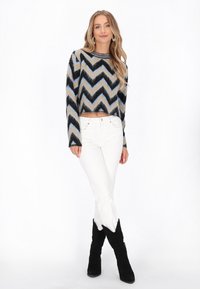 Pada žaketo su kirpimu, purvinas megztinis su mėlynu, juodu ir smėlio spalvos zigzagu; derinamas su baltais džinsais ir juodais zomšos iki kelių batais.