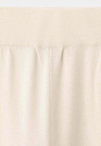 Gros plan d'un tissu tricoté de couleur crème montrant une ceinture côtelée et une couture verticale dans un matériau doux et texturé.