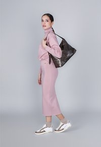 Maglione rosa chiaro e gonna coordinata con un design aderente, abbinati a sneakers bianche e una borsa tote marrone scuro. Texture liscia in tutto.