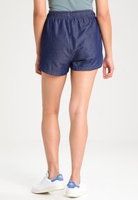 Shorts en denim avec une taille élastique, de couleur bleu foncé, présentant une coupe décontractée et une texture lisse. Portés avec des baskets blanches.