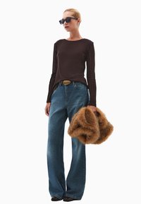 Langdurige mouw bruin top, blauwe wijde jeans, bruin bontaccessoire, zwarte zonnebril, gladde textuur, eenvoudig ontwerp, en gouden riemaccent.