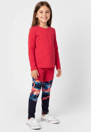 Czerwony top z długim rękawem zestawiony z wielokolorowymi legginsami z wzorem flamingów i ciemnoniebieskimi akcentami. Dopełnieniem stroju są białe trampki.