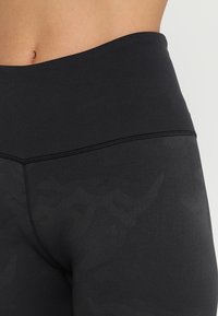 Czarnie legginsy o wysokim stanie, wykonane z gładkiego materiału z delikatnym wzorem kamuflażu; posiadają wzmocnione szwy wzdłuż pasa i szwów.