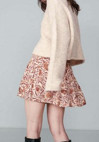 Pull en tricot crème associé à une mini-jupe à motifs floraux dans des nuances d'orange et de rose. La jupe a une coupe évasée avec des plis.