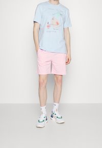 T-shirt en coton bleu clair avec imprimé graphique, associée à un short rose clair. Baskets blanches avec des accents verts et bleus, chaussettes blanches.