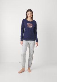 Granatowa bluzka z długim rękawem z wzorzystym frontem, w połączeniu z jasnoszarymi spodniami dresowymi z detalem w postaci bocznego paska. Wygodny krój, casualowy design.