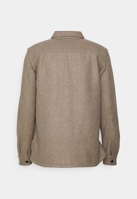 Veste-chemise en laine beige à manches longues, dos droit, poignets boutonnés et col classique sur fond blanc.