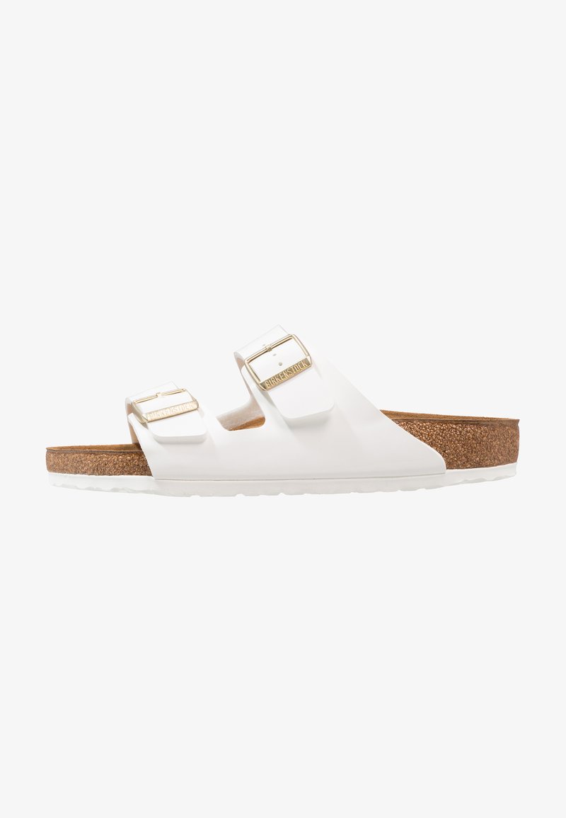 Weiße Gummisandalen mit zwei verstellbaren Riemen, goldenen Schnallen und einem braunen Korkfußbett. Strukturiertes Profil für besseren Grip, minimalistisches Design.