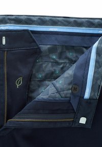 Marineblaue Stoffhosen mit einem gefütterten Karomuster in Türkis, goldener Reißverschluss und einem in Grün gestickten Blätter-Logo.
