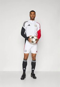 Futbola tērps melnā, baltā un sarkanā krāsā. Ar garām piedurknēm, komandas logotipiem un melnām zeķēm ar trim baltām svītrām. Tur futbolbola bumbu.