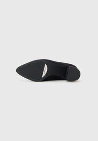 Black suede high-heeled shoe sole, pointed toe design, smooth upper, rubber outsole with grips, and metallic branding detail visible.