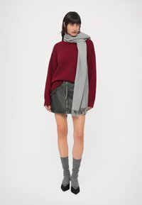 Camisola de malha bordeaux, cachecol cinzento com franjas, saia de couro preta com fechos éclair, meias cinzentas caneladas e saltos pretos pontiagudos. Design simples e moderno.