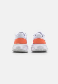 Un par de zapatillas deportivas blancas con acentos naranjas en el talón, mostradas desde atrás sobre un fondo blanco liso.