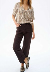 Kortärmad, beige topp med ormtryck som bärs tillsammans med mörkbruna högmidjade jeans och mönstrade loafers i nyanser av beige och brunt.