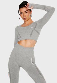 Gray long-sleeve crop top with cutout and textured sleeves, paired with high-waisted gray leggings featuring a white logo and accent lines.