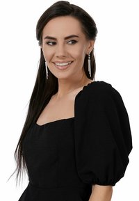 Svart klänning med puffärmar och fyrkantig halsringning, i texturerad tyg, samt hängande diamanörhängen som framhäver en modern design.