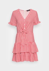 Robe en vichy rouge et blanc avec de courtes manches volantées, un devant noué et une jupe à volants. Fabriquée en tissu léger, elle présente une fermeture à boutons.