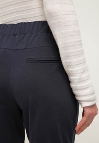 Námořnické modré kalhoty z elastického materiálu s elastickým pasem, obsahující malou, horizontální zadní kapsu a hladkou texturu.