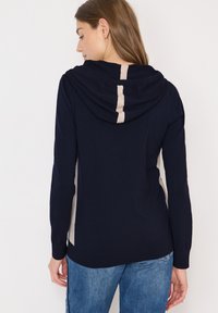 Marineblauwe hoodie met een beige verticale streep op de achterkant; heeft een gestructureerde stof en ribgebreide mouwen en onderkant.