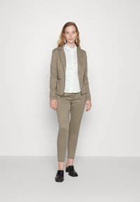 Bruin geblokt tailor made colbert met bijpassende slim-fit broek, gecombineerd met een wit overhemd met kraag en zwarte instappers.