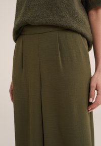 Olive green, wide-leg trousers made of a soft, textured fabric with pleats at the front and a smooth waistband.