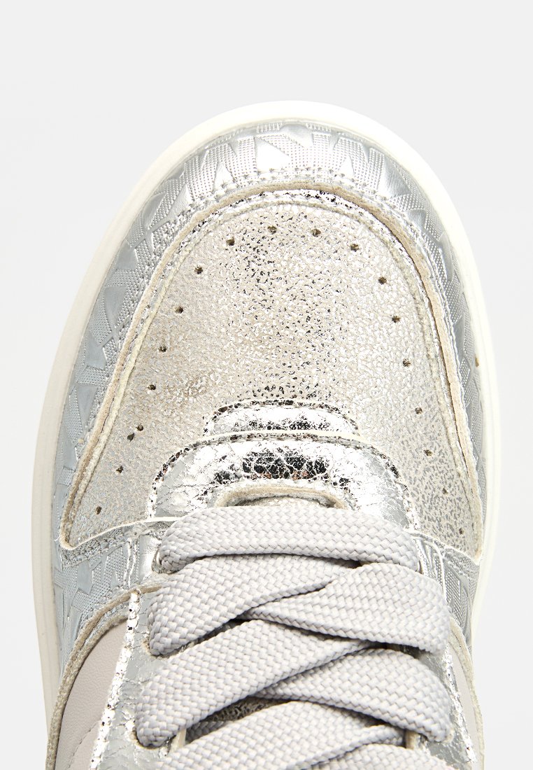 Zapatilla metálica plateada con superposición texturizada, que presenta cordones grises y una suela lisa. Acentuada con perforaciones y patrones geométricos.