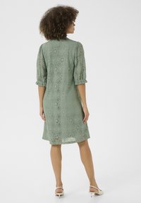 Müntroheline pitskleit, millel on lillemuster, puffpuhvis varrukad ja lõdvestatud istuvus, ulatudes keskmiselt reieni, koos heledate kontsakingadega.