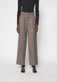 Grå, vida byxor med veck och hög midja. Tillverkade av ett strukturerat tyg. I kombination med svarta klackskor. Långärmad svart topp.