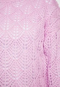 Maglione all'uncinetto di colore rosa chiaro con un motivo a diamante, caratterizzato da una texture aperta e ariosa e da cuciture intricate in tutto il capo.