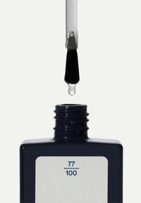 Flacon de vernis à ongles avec un corps carré bleu foncé, étiquette blanche marquée "77/100", pinceau noir au-dessus avec une goutte de vernis.