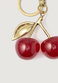 Μπρελόκ με δύο λαμπερές κόκκινες γυαλιστερές κερασιές προσκολλημένες σε χρυσό μεταλλικό στέλεχος και φύλλο σε απλό ανοιχτό φόντο.