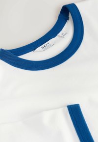 T-shirt bianco con scollo a costine blu e tasca. L'etichetta visibile all'interno del colletto indica "NEXT" e taglia "M." Tessuto in cotone morbido.