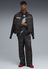 Jachetă și pantaloni de curse negri cu cusături și accente roșii, având un logo Formula 1. Design elegant cu o croială modernă și textură din țesătură.