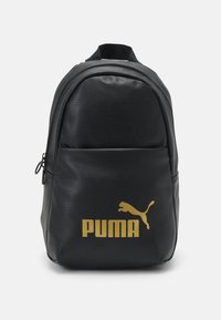 Czarny plecak o gładkiej, teksturowanej powierzchni. Posiada wyraźne złote logo Puma oraz kieszeń na zamek z przodu. Klasyczny, zaokrąglony kształt.