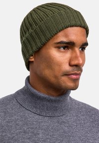 Berretto lavorato a maglia verde con motivo a coste orizzontali, abbinato a un maglione grigio a collo alto. Il cappello si adatta bene alla testa.