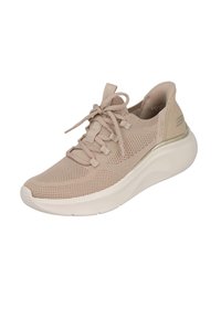 Zapatilla deportiva beige con parte superior de malla transpirable, diseño texturizado, parte frontal con cordones y una suela blanca gruesa con una curva sutil.