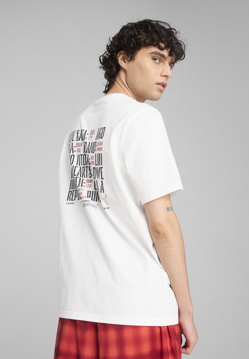 Witte katoenen T-shirt met een grafische print op de achterkant, voorzien van verschillende textelementen in het zwart en rood. Korte mouwen en een relaxte pasvorm.