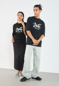 Svart oversized t-skjorter med Mickey Mouse-grafikk, sydd sammen med et svart denimskjørt og lyseblå vide jeans. Rutete slip-on sko.