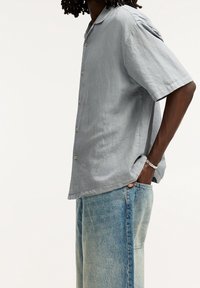 Camisa de botón de manga corta, de color gris claro, fabricada con una tela texturizada, combinada con jeans de tiro alto de color azul claro con un acabado deslavado.