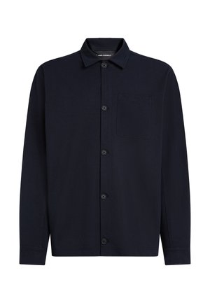 Tumši zila garām piedurknēm krekls no mīksta auduma, ar pogu aizdari priekšpusē, izteiktu apkakli un vienu kabatu uz kreisās krūšu puses.