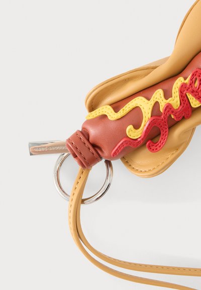 Porte-clés en cuir en forme de hot-dog avec détails moutarde et ketchup, anneau en métal attaché et sangle beige.