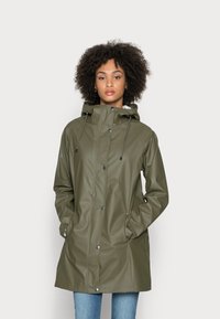 Olijfgroene regenjas met een capuchon, gemaakt van waterdicht materiaal. Voorzien van drukknoopsluitingen, trekkoorden en zijzakken. Glad textuur.