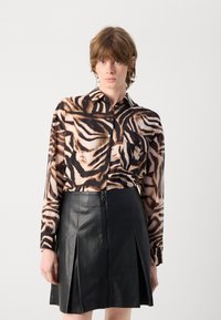 Camicia a maniche lunghe con un motivo a strisce di tigre marroni e nere, abbinata a una gonna in pelle nera a vita alta con cerniera frontale.