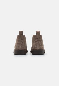 Botas de tobillo de ante marrón con un patrón de puntos texturizados, un tacón bajo y lengüetas en la parte posterior para ponérselas fácilmente.