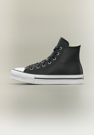 Baskets montantes noires avec bout et semelle en caoutchouc blanc, lacets noirs et œillets métalliques, présentées de profil sur un fond neutre.